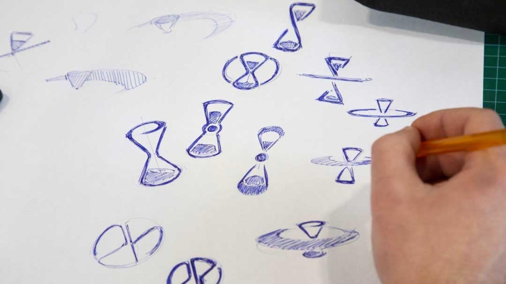 Personne qui dessine des sabliers au stylo bleu sur une feuille blanche